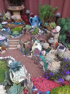 a garden filled with lots of different types of plants and rocks next to a red fence