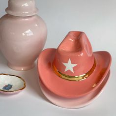 a pink hat sitting on top of a plate next to a white vase and bowl