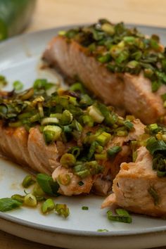 two pieces of fish on a plate with green onions and pistachio sprinkles