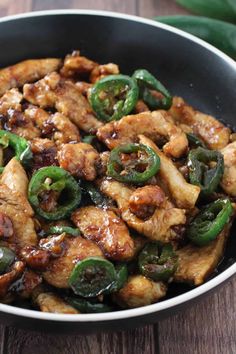 chicken and peppers in a skillet on top of a wooden table next to a green pepper