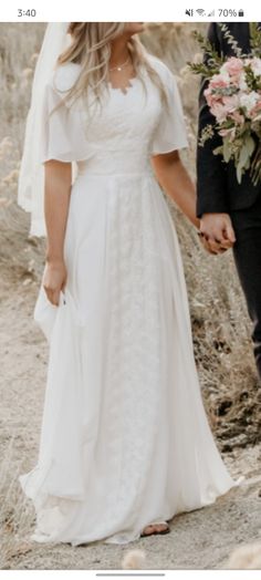 a bride and groom holding hands while walking down a path in the desert with flowers on either side