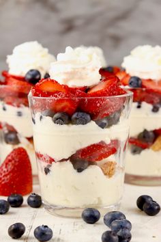 three desserts with strawberries, blueberries and whipped cream in them on a table