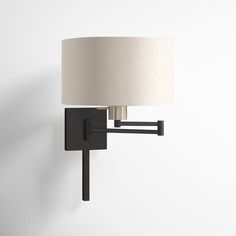 a black wall light with a white shade on it's arm and a lamp attached to the wall