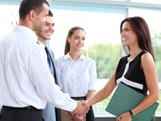 two business people shaking hands in an office setting with three other people standing around them