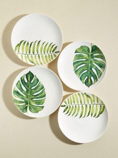 three white plates with green leaves painted on the front and back of them, sitting on a beige surface