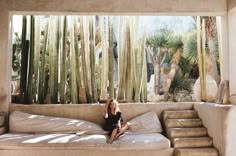 a woman sitting on top of a couch in front of a window filled with plants