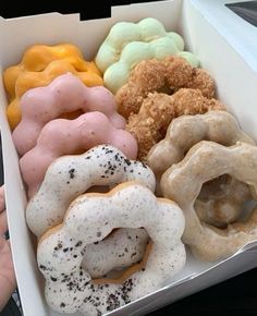 a box filled with different flavored donuts on top of a table next to a person's hand