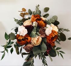 a bridal bouquet with orange and red flowers on white table cloth, eucalyptus leaves and greenery