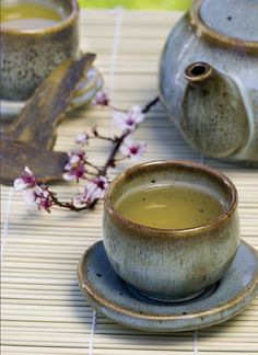 two tea cups and saucers sitting on a bamboo mat with flowers in the background