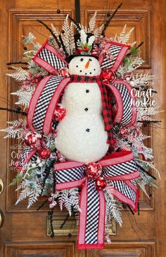 a snowman wreath with red and black ribbon hanging on a wooden front door,