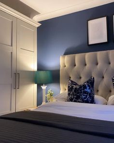 a bedroom with blue walls and white bedding, two framed pictures on the wall