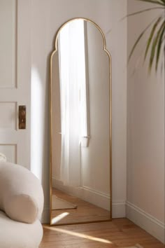 a large mirror sitting on top of a wooden floor next to a white chair and potted plant