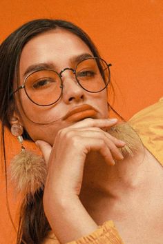 a woman wearing glasses and holding her hand to her face, with an orange background