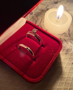 two wedding rings in a red velvet box next to a candle