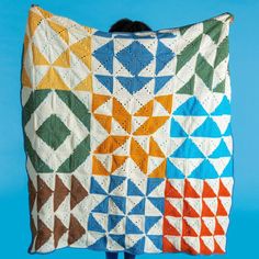 a person holding up a colorful quilt on top of a blue background with an orange, yellow, green, and red design