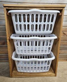 three white laundry baskets stacked on top of each other in front of a wooden shelf