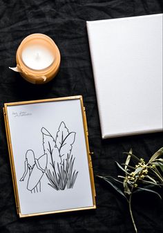 a candle and some plants on a black cloth with a white box next to it