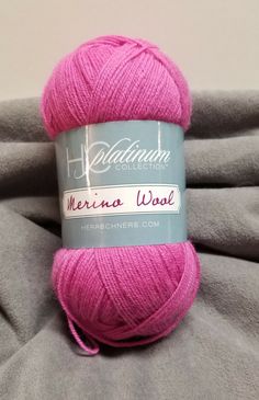 a pink ball of yarn sitting on top of a gray blanket with the words merano wool