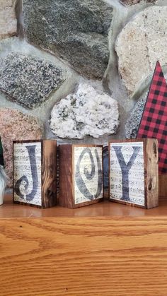 three wooden blocks that spell out the word joy on top of a table next to a stone wall