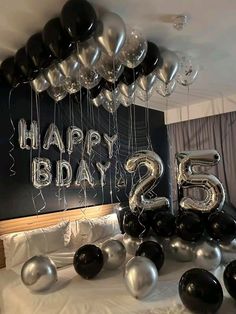 black and silver balloons in the shape of numbers sit on a bed next to a chalkboard that says happy bday