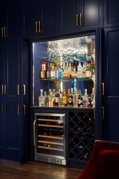 a wine rack with bottles and glasses on it next to a red chair in front of a blue cabinet