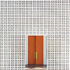 an orange door is in front of a white lattice - like wall with gold handles