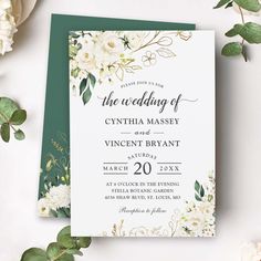 an elegant wedding card with white flowers and greenery