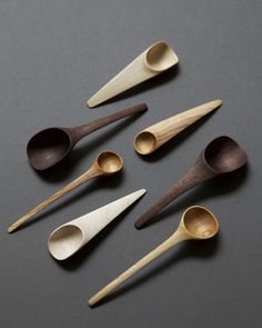 six wooden spoons lined up next to each other on a gray surface with black background