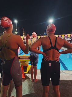 two women in swimsuits standing next to each other near a swimming pool at night