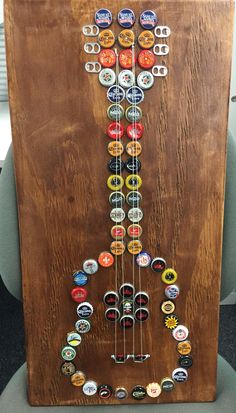 a guitar made out of beer bottle caps on top of a wooden plaque with the letter j