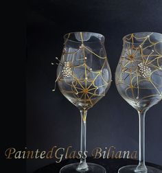 two wine glasses with designs on them sitting side by side in front of a black background