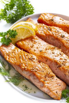 two pieces of salmon on a plate with lemon and parsley