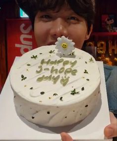 a young boy holding a cake with the words happy birthday written on it in front of his face