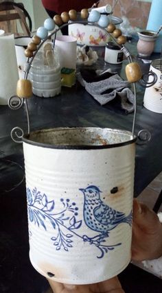 a hand holding a white bucket with blue birds painted on it and beads around the rim