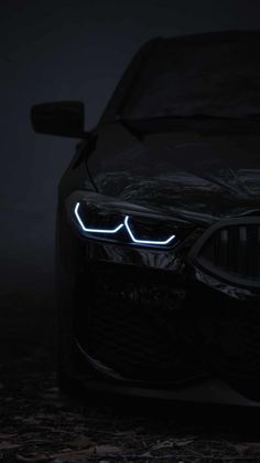 the front end of a black car with its lights on in the dark, it is glowing