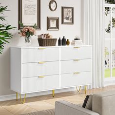 a living room with white furniture and pictures hanging on the wall above it's dresser