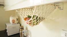 fruit in a net hanging from the side of a kitchen counter next to a blender