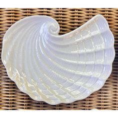 a white shell shaped dish sitting on top of a wicker table