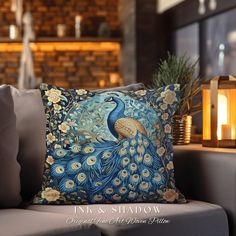 a blue and gold pillow with a peacock on it sitting on a couch in front of a brick wall