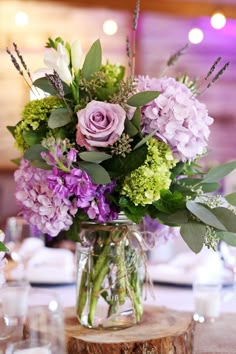 a vase filled with purple and green flowers on top of a wooden table next to glasses