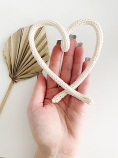 a hand holding a heart shaped knot with a fan behind it on a white surface