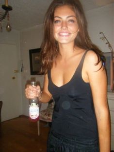 a young woman holding a bottle of alcohol in her right hand and smiling at the camera