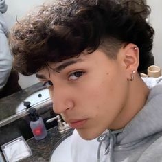 a young man with curly hair is looking at the camera while wearing earrings