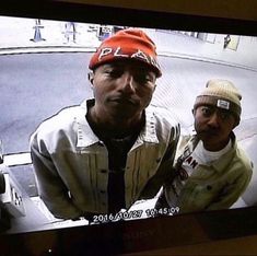 two men are on the television screen with one man wearing an orange hat and another is looking at the camera