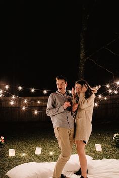 a man and woman standing next to each other in front of string lights on the ground