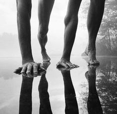 the legs and feet of two people standing in water with their reflection on the ground