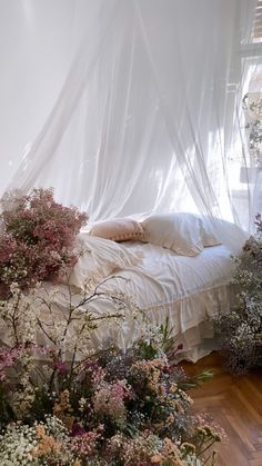 an unmade bed with white sheets and flowers on the floor in front of a window