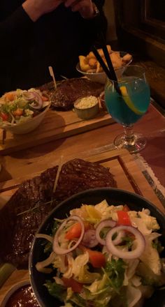 a table topped with plates and bowls filled with food next to glasses of water on top of wooden trays