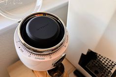 a white coffee maker sitting on top of a wooden table next to a window sill