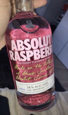 a bottle of absolut raspberry vodka is being held up by someone's hand